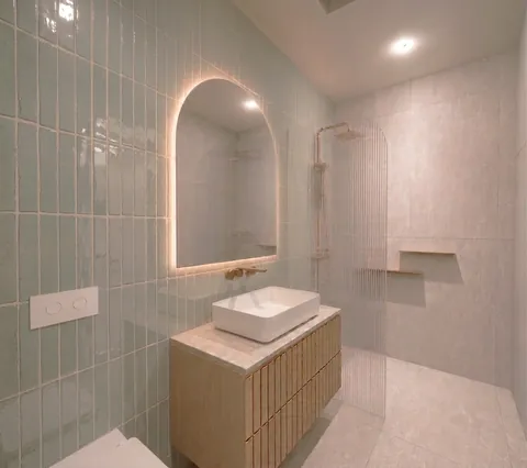 Architectural render: Bathroom with green vertical tiles, a backlit arched mirror and fluted glass shower screen – duplex in Sylvania