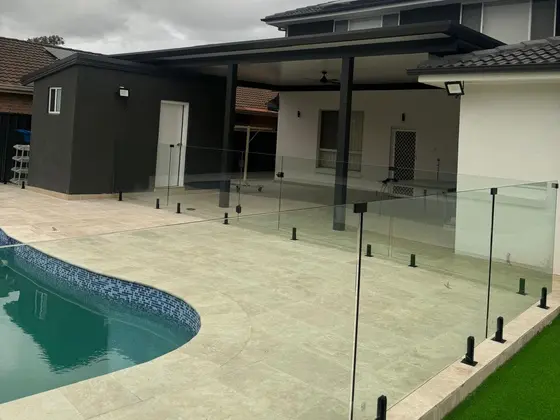 Pool with pale paving and frameless glass fencing beside the covered outdoor area of a renovated home in Chipping Norton by St Anthony Building Group